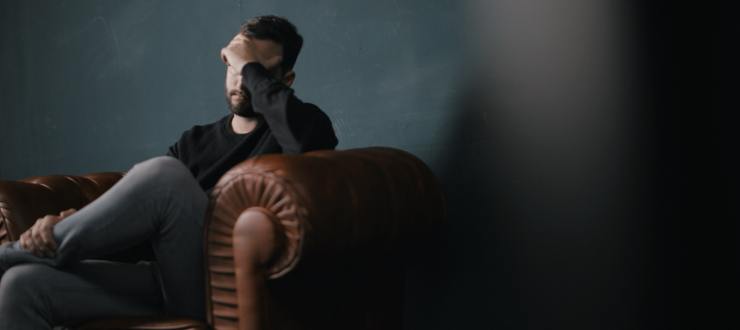 A male energy customer in need of support sits on a sofa with his head in his hands